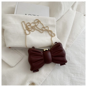 Détail du mini sac bordeaux en forme de nœud avec chaîne dorée sur fond texturé blanc