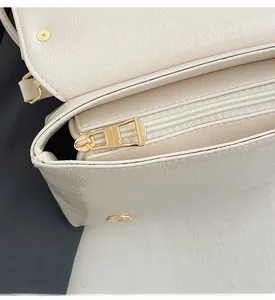 Macro shot of smooth gold zipper and magnetic clasp on cream leather shoulder bag