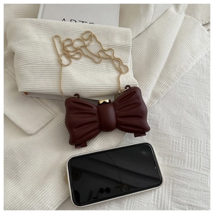 Gros plan d'un mini sac nœud bordeaux avec chaîne dorée sur fond en tricot blanc