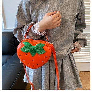 Détail du sac bandoulière orange en forme de fraise avec feuilles vertes sur modèle