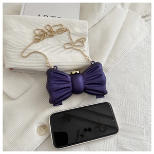 Vue détaillée d'une pochette nœud violette avec chaîne dorée à côté d'un smartphone