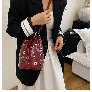 Detail of burgundy drawstring bucket bag with shiny metallic grommets and silver studs