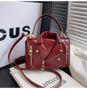 Detail of burgundy patent leather jacket-style bag with gold rivets and zippers