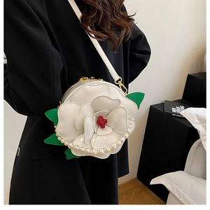 Detail of white camellia floral evening bag with pearl trim and green leaf accents