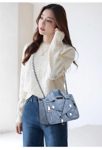 Detail of blue denim crossbody bag featuring moto jacket design and metal chain strap