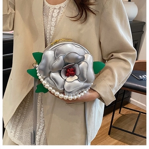 Detail of silver camellia flower crossbody bag with pearl handle and green leaves