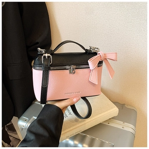 Detail of pink and black leather handbag featuring litchi texture and side bow accent