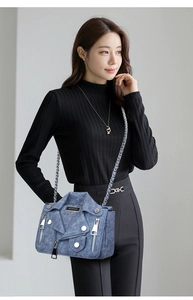 Detail of blue denim crossbody bag featuring moto jacket design and silver studs