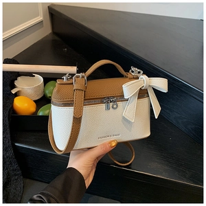 Detail of two-tone crossbody box bag with bow decoration and metal zipper closure