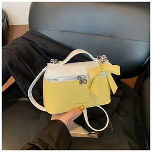 Detail of yellow and white crossbody bag featuring a leather bow and embossed fashion text