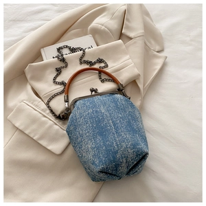 Detail of blue denim bucket bag with bronze metal clasp and brown leather handle