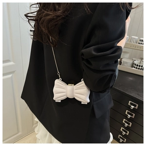 Détail d'un sac à chaîne blanc en forme de nœud porté sur un blazer noir et jupe blanche