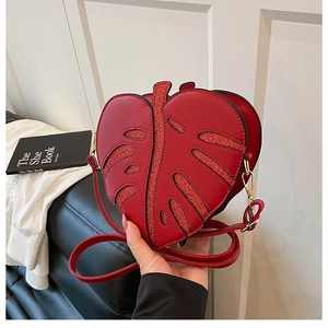 Close-up of red leaf-shaped crossbody bag featuring glittery leather and golden hardware