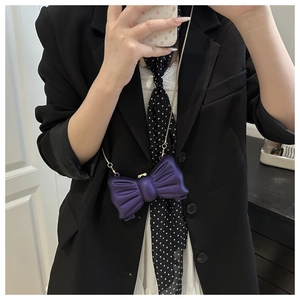 Détail d'un mini sac violet en forme de nœud avec chaîne dorée sur une tenue chic