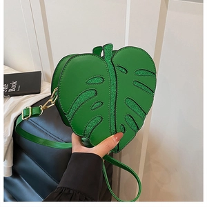 Detail of leaf-shaped green shoulder bag with glitter veins held by a hand