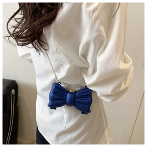Détail d'un mini sac bandoulière bleu marine en forme de nœud avec chaîne dorée sur mannequin