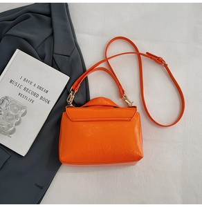 Detail of bright orange crocodile pattern crossbody bag with golden hardware and strap