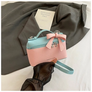 Detail of light blue and pink bow handbag with litchi grain texture and long strap