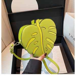 Detail of lime green leaf-shaped bag with fine stitching and gold hardware in a gift box