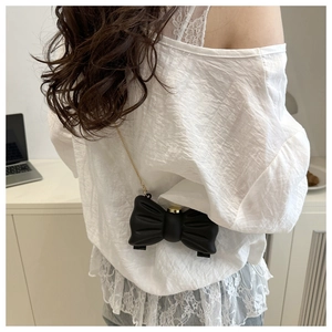 Détail d'un sac à bandoulière noir en forme de nœud avec chaîne dorée et finition mate