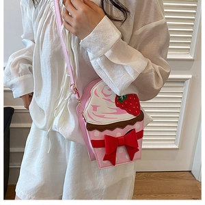Detail of pink cupcake-shaped crossbody bag with strawberry top and red bow detail