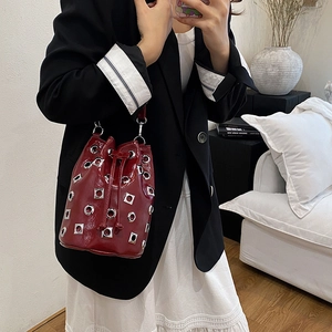 Sac seau rouge verni avec rivets argentés et cordon, porté dans un décor minimaliste