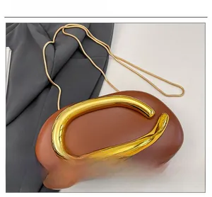 Detail of a brown pebble leather clutch bag featuring a polished gold C-shape buckle