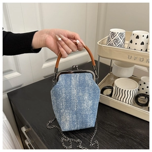 Detail of denim doctor bag featuring metal clasp and brown leather handle with chain strap