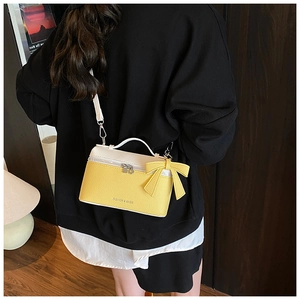 Detailed shot of yellow and white crossbody bag with bow and litchi texture