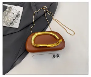 Brown semi-circle evening bag with wavy gold metal handle and chain next to a phone