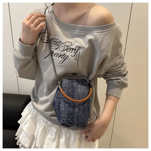 Denim clasp bag with brown round handle and chain strap worn with off-shoulder gray sweatshirt