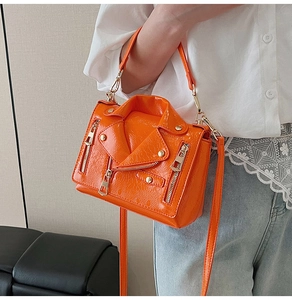 Detail of bright orange jacket-shaped crossbody bag featuring metallic zippers and buckles