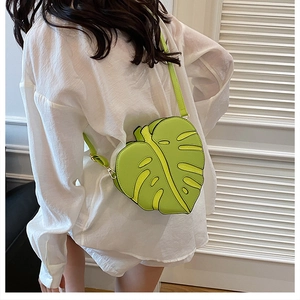 Detail of creative green monstera leaf shaped crossbody bag worn over a white shirt