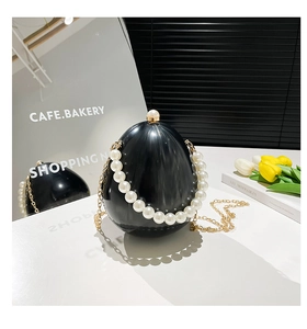 Dettaglio di una pochette in acrilico nero a forma di uovo con manico di perle e catena
