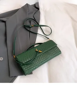 Détail d'un sac tressé vert foncé avec boucle à nœud doré et fine bandoulière en cuir