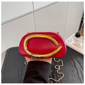 Detail of red acrylic evening bag featuring a gold C-shaped clasp and snake chain strap
