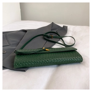 Détail de la texture en cuir tressé vert foncé et boucle dorée d'un sac bandoulière