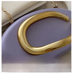 Detail of purple leather clutch bag with a large gold C-shaped metal handle and chain strap