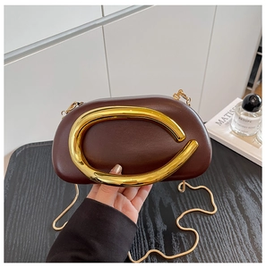 Macro detail of the C-shaped golden metal handle on a dark brown leather clutch bag
