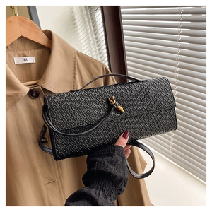 Détail du sac bandoulière tressé noir avec fermoir tournant doré sur fond de lumière douce