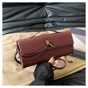 Détail de la pochette tressée bordeaux avec fermoir nœud doré et rabat élégant