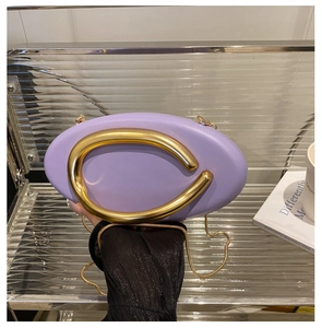 Detail of purple oval clutch bag featuring a prominent gold C-shaped metal handle and chain