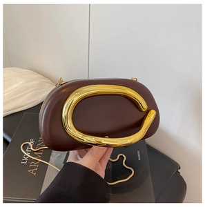 Detail of dark brown oval clutch bag with large golden C-shaped buckle and metal chain