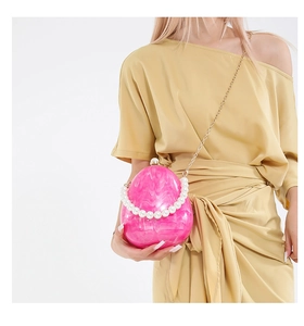 Dettaglio della clutch fucsia a forma di uovo in acrilico marmorizzato con manico di perle