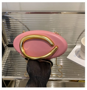 Close-up of pink round evening clutch with gold metal ring handle and chain strap