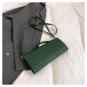 Détail du sac bandoulière tressé vert foncé avec crochet doré sur un blazer