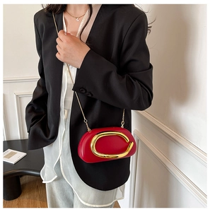 Detail of red acrylic evening bag with gold C-shaped buckle and metal chain strap