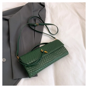 Détail du sac tressé vert foncé avec boucle dorée en nœud sur tissu de coton blanc