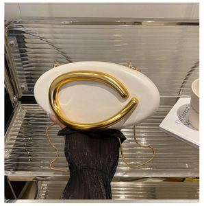 Detailed close-up of white leather clutch bag featuring a unique gold curved handle