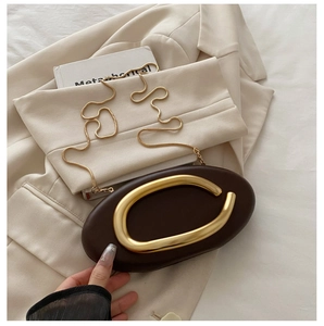 Detail of a dark brown oval evening bag with a gold C-shaped handle on a beige blazer